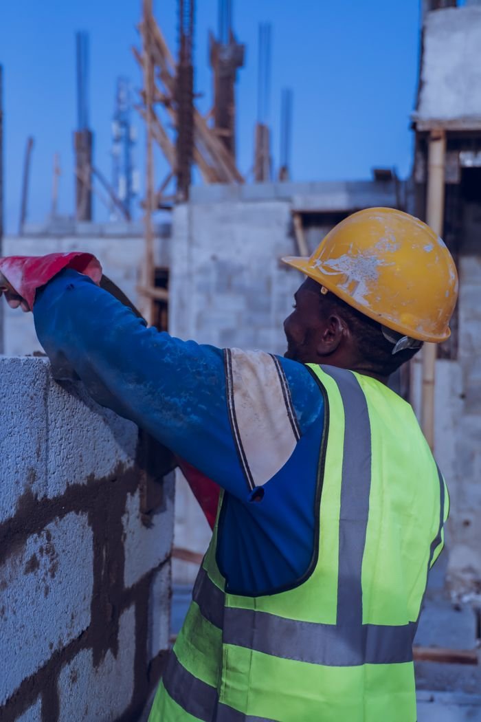 Construction worker in safety gear building a concrete wall at an outdoor site.